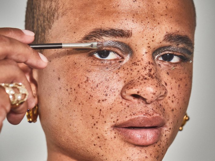 person applying metallic silver eyeshadow to their eyelid with a brush