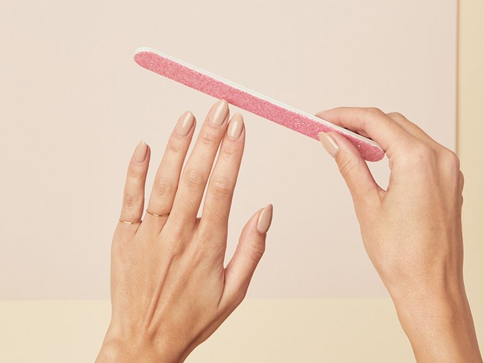 Close-up of person's hands holding a pink nail file to one hand