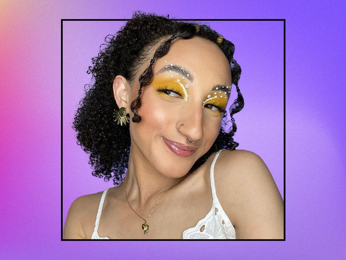 A photo of a person with brunette curly hair wearing electric yellow eyeshadow with pearl appliques.