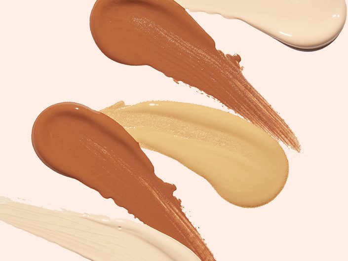 Swatches of different shades of foundation on a light pink surface