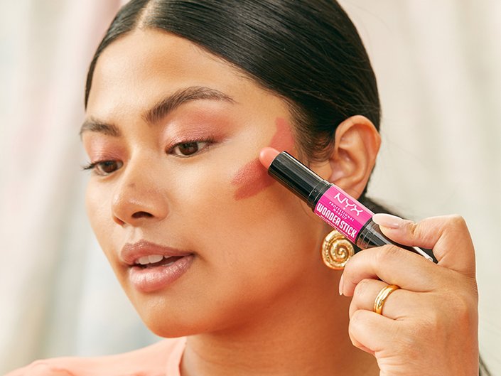 Person looking down and applying the NYX Wonder Stick Blush to their face to contour their cheekbones