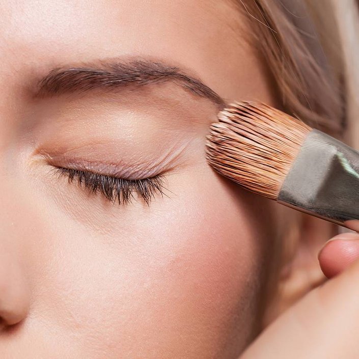 close-up of hand applying makeup to person's face with a makeup brush