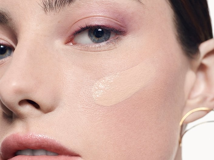 Swatches of different shades of liquid foundation on a green background.